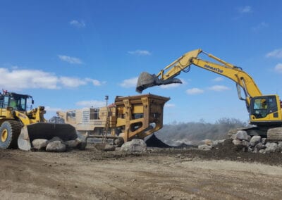 Loader carrying rocks and excavator putting it in crusher